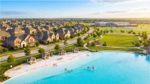 Aerial view of a master-planned community in North Texas with a crystal-clear lagoon, white sand beach, family park, and a modern school building in the background
